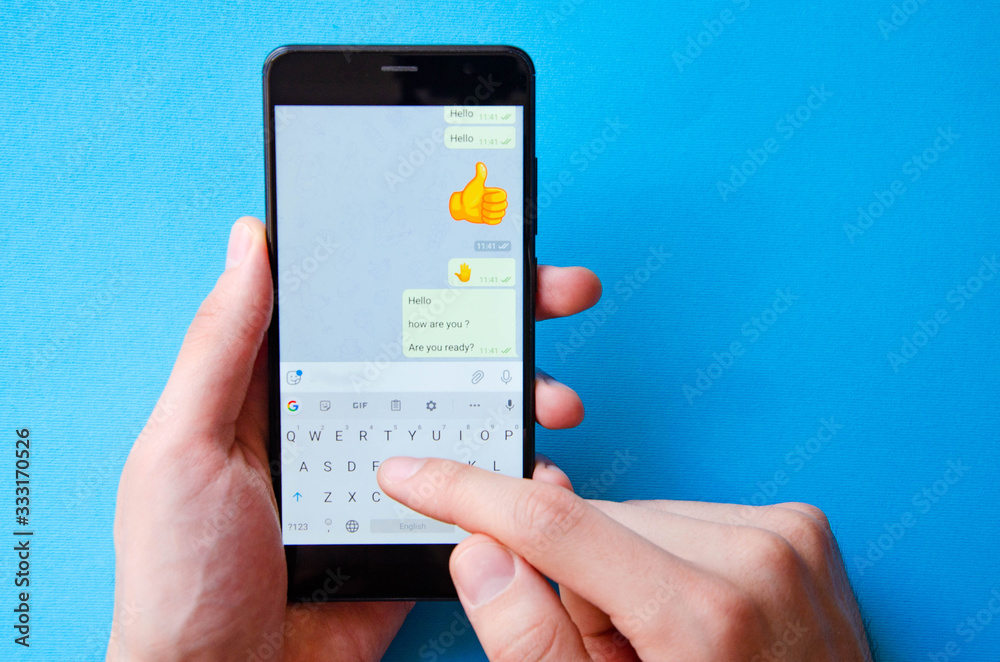 A male hand holds a smartphone, points a finger, types. Communication on a smartphone, correspondence. Place for text. Smartphone in hand on a blue background. A male hand holds a smartphone, points a finger, types. Communication on a smartphone, correspondence. Place for text. Smartphone in hand on a blue background.