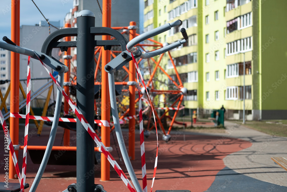 Coronavirus COVID-19 restriction. No people due to quarantine. Closed children's playground in the city. Empty park and playground. Stay at home compaign. Red warning tape on swings and slides