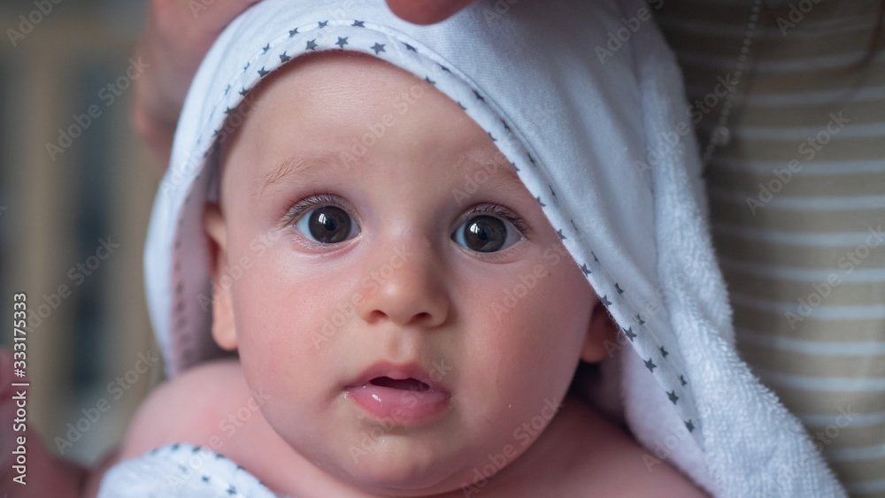 Authentic close up shot of a cute newborn baby in a white bathrobe is held by his mother after bathing and smiling in the camera. Concept of children,baby, parenthood, childhood, life Authentic close up shot of a cute newborn baby in a white bathrobe is held by his mother after bathing and smiling in the camera. Concept of children,baby, parenthood, childhood, life