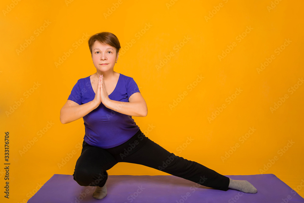 Aged woman doing yoga on a purple rug. Studio photo on a yellow background. Aged woman doing yoga on a purple rug. Studio photo on a yellow background.
