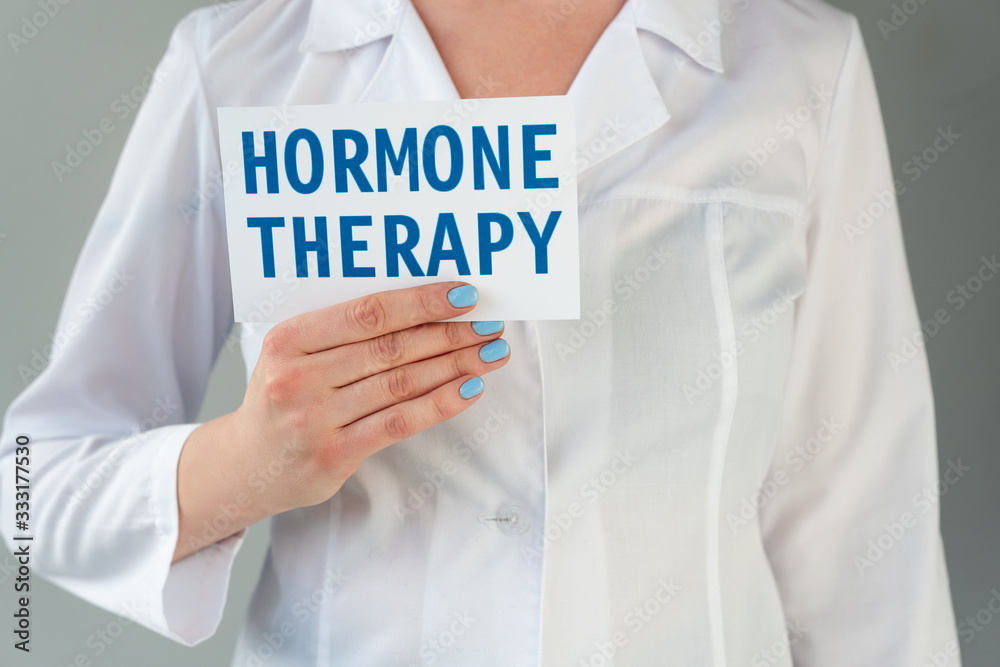 Cropped view of doctor in white coat holding card with hormone therapy lettering isolated on grey Cropped view of doctor in white coat holding card with hormone therapy lettering isolated on grey