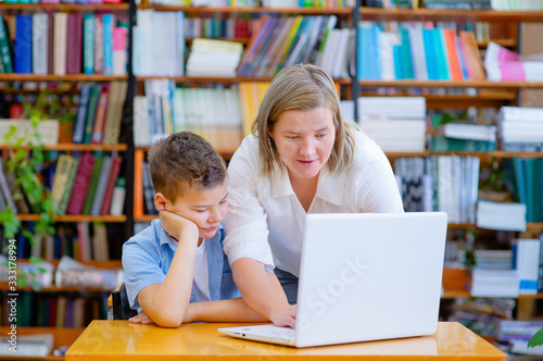 Mom or teacher working with a school boy on the computer in the library.