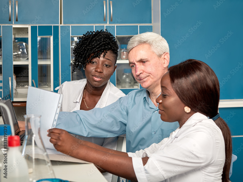 Obraz premium Female African medical students or young graduates discuss with Caucasian senor male group leader in research or medical laboratory. Looking for treatment, developing vaccine for Covid-19.pandemic
