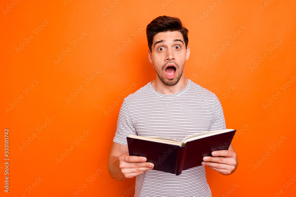 Photo of funny attractive guy hold favorite book hands reading exciting final intrigue open mouth unexpected happening wear striped t-shirt isolated bright orange color background Photo of funny attractive guy hold favorite book hands reading exciting final intrigue open mouth unexpected happening wear striped t-shirt isolated bright orange color background