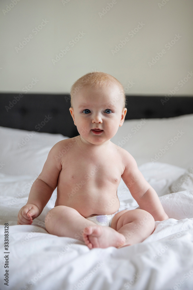 Cute baby wearing a nappy sat on a bed looking at the camera Cute baby wearing a nappy sat on a bed looking at the camera