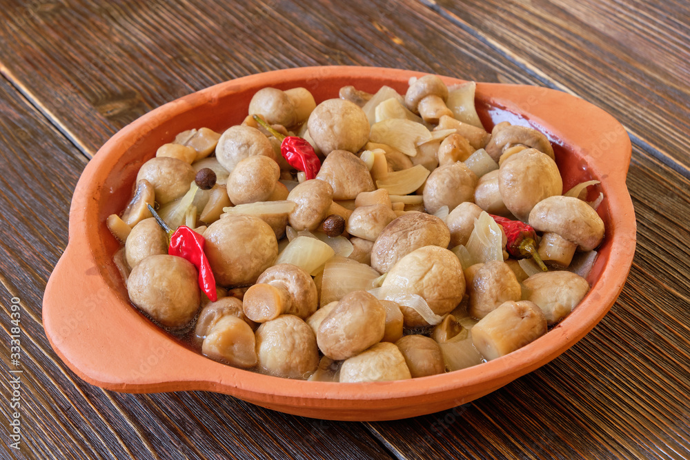 Clay bowl with pickled mushrooms on a light wooden table Clay bowl with pickled mushrooms on a light wooden table
