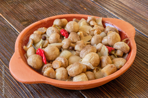Clay bowl with pickled mushrooms on a light wooden table