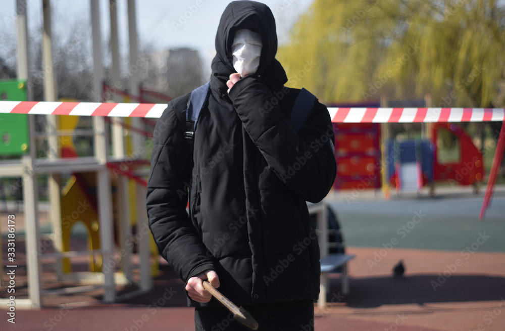 A man in the hood with a crowbar stands on the background of a signal tape in the park A man in the hood with a crowbar stands on the background of a signal tape in the park