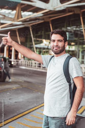 Cheerful young man trying to stop car. Smiling young man showing thumb up. Travel concept
