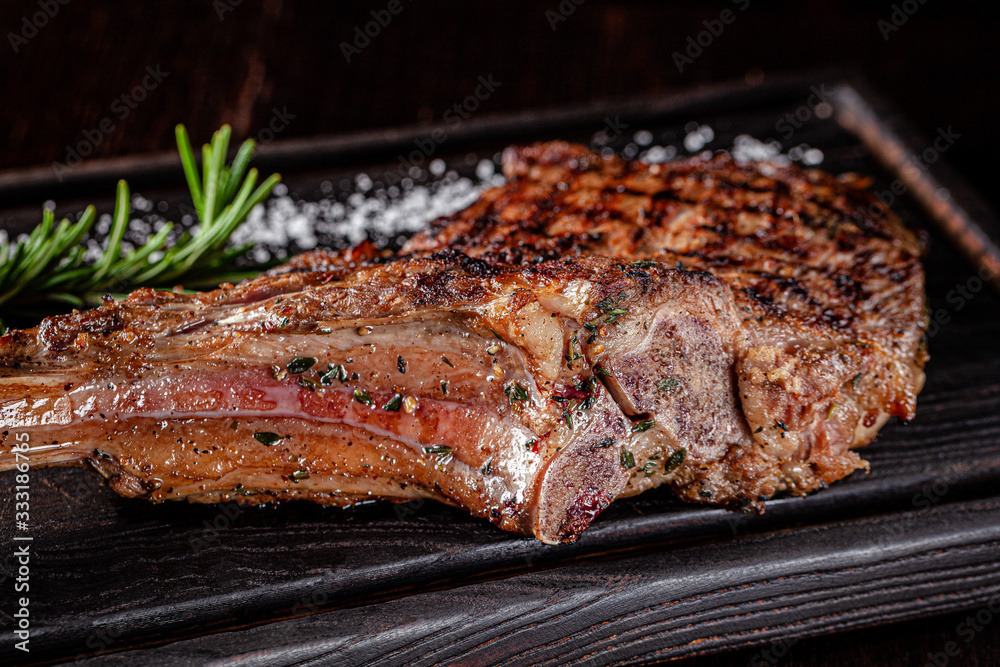 American cuisine. Large juicy grilled steak on a tomahawk bone. Beef steak on a wooden board with rosemary and salt. background image, copy space text