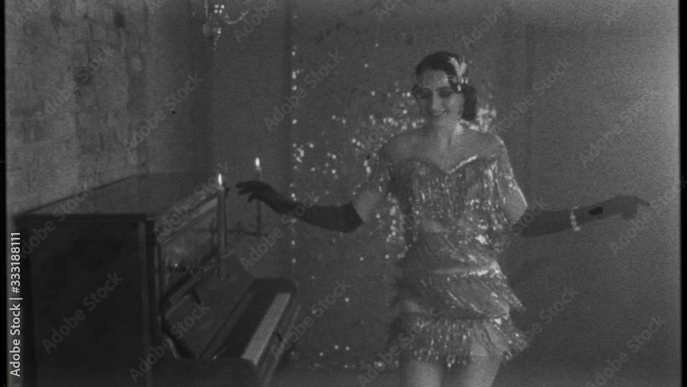 Young happy beautiful woman in bright sparkling luxury silver dress, smiles gown fluttering dances in room near piano, black and white old fashioned film with added noise. 20s stylized carnival party