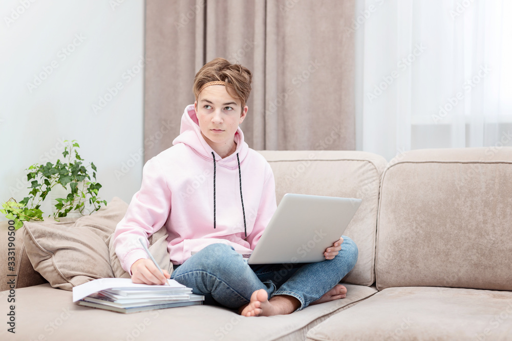 Online education. Distance learning. Self-isolation. Learning at home. Schoolboy studying at home with a computer. homework.Sitting on sofa with training books Online education. Distance learning. Self-isolation. Learning at home. Schoolboy studying at home with a computer. homework.Sitting on sofa with training books