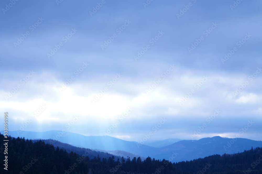 View of autumn mountains with trees without leaves under a cold gray sky and heavy white clouds View of autumn mountains with trees without leaves under a cold gray sky and heavy white clouds