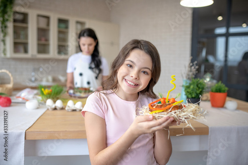 Smiling girl in jeans standing in the kitchen and holding easter bun in her hands