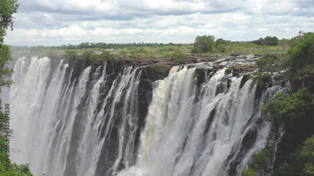 Victoria Falls at the Zambia Zimbabwe boarder with blue sky and white clouds and water cascading over the cliff. Victoria Falls at the Zambia Zimbabwe boarder with blue sky and white clouds and water cascading over the cliff.