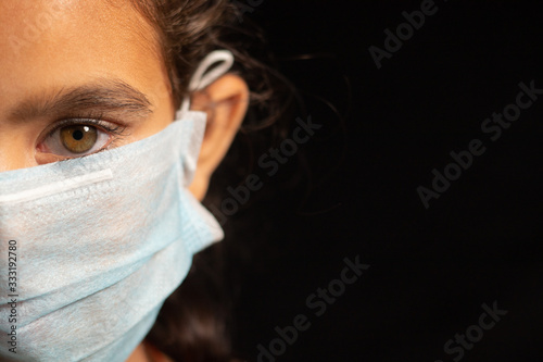young girl child with medical mask wearing, protection against covid 19 or coronavirus pandemic on black background with copy space.