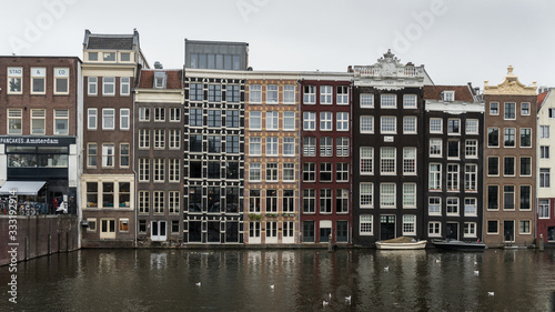 Old houses in central Amsterdam near water іn a cloudy day.