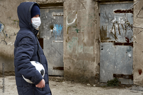 concept of epidemic and quarantine - a boy with a face mask and a ball alone on the street in the city © soleg