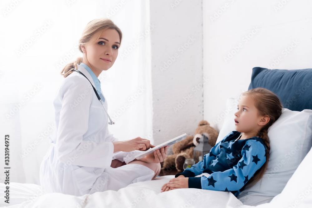 attractive doctor in white coat using digital tablet near sick kid attractive doctor in white coat using digital tablet near sick kid
