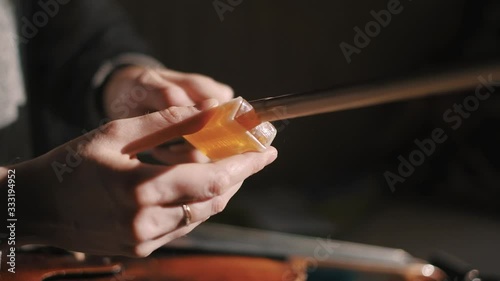 Young woman fiddler applying rosin to the violin bow hair to create friction between the bow and the strings, closeup shot, dust specks particles floating in air