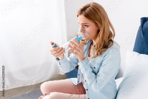 asthmatic woman using inhaler with spacer in bedroom