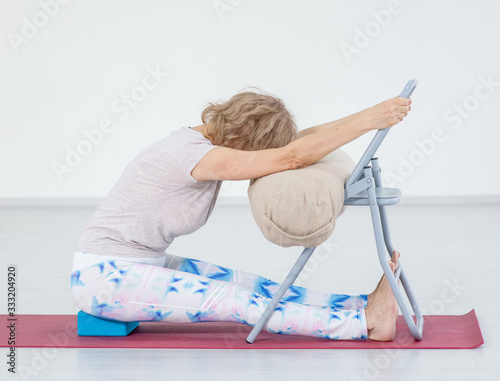 Принти на полотні Senior woman doing yoga with chair in a gym. Stretching exercises