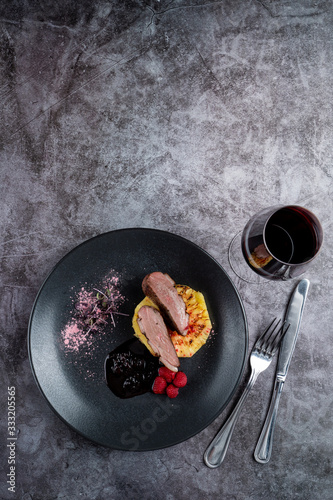 Top view of duck breast with baked pineapple and raspberry on grey stone background, copy space