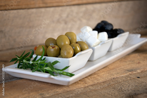 Platter of olives, feta cheese and rosemary on wooden board