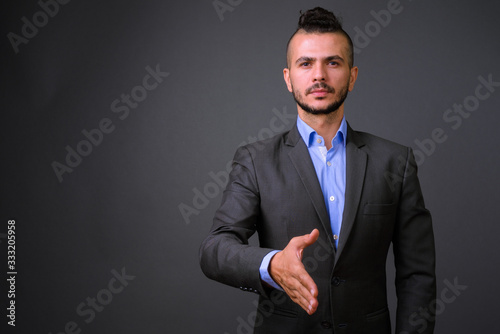 Portrait of handsome bearded Turkish businessman in suit giving handshake