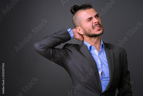 Portrait of stressed bearded Turkish businessman in suit having neck pain