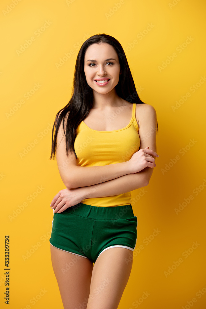 attractive smiling girl in green shorts standing with crossed arms on yellow attractive smiling girl in green shorts standing with crossed arms on yellow