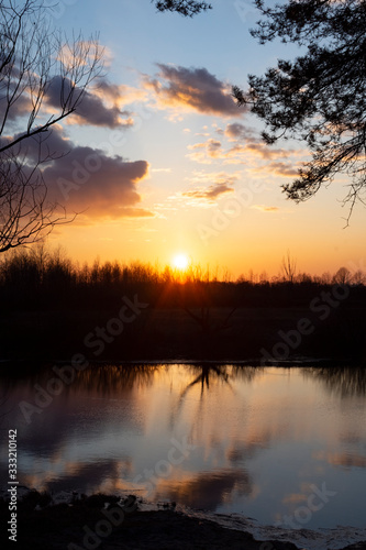 Fototapeta Naklejka Na Ścianę i Meble -  The sun in the cloudy sky. Sunset by the river near the forest.
