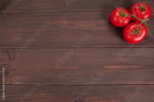 Branch with three ripe red tomatoes on rustic wooden background with copy space. Fresh vegetables, top view