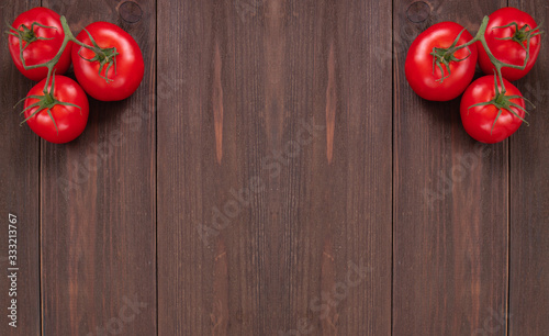 Two branches with three ripe red tomatoes on rustic wooden background with copy space. Fresh vegetables, top view