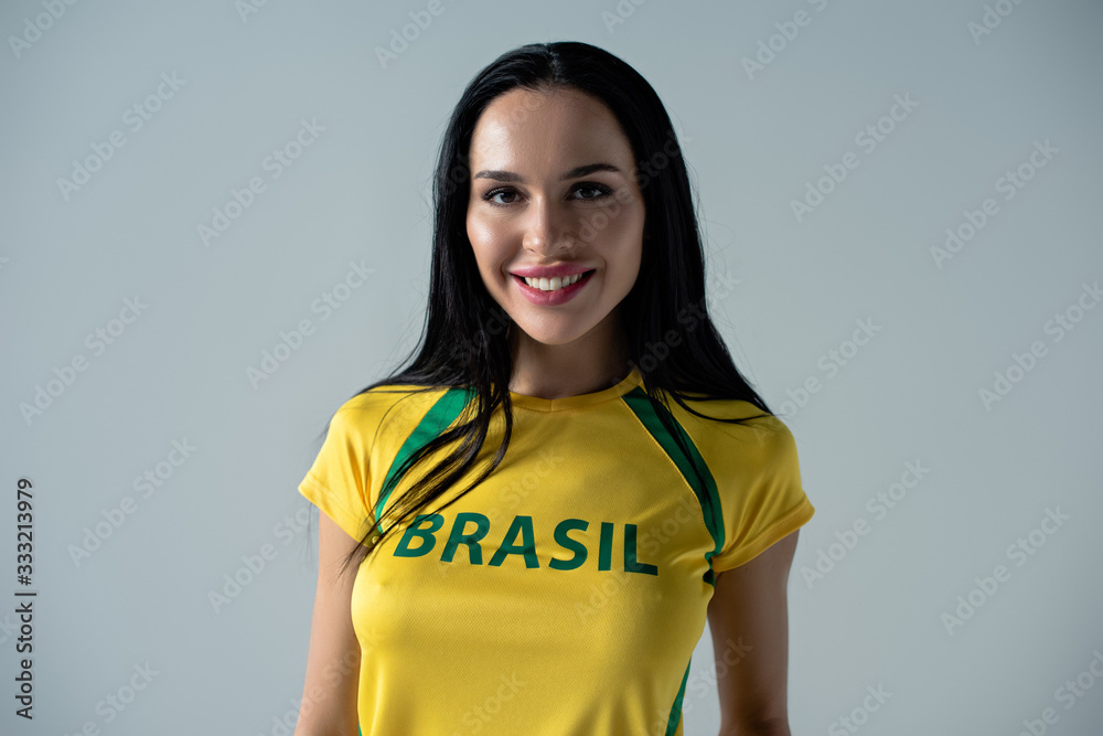 smiling female football fan in yellow t-shirt with brazil sign isolated on grey smiling female football fan in yellow t-shirt with brazil sign isolated on grey
