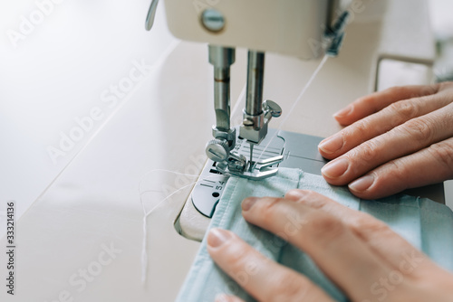 Woman hands using the sewing machine to sew the face home made diy medical mask during the coronavirus pandemia.