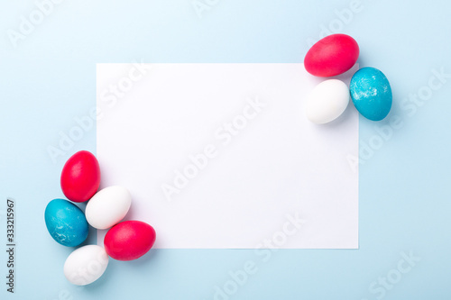 Spring mockup with Easter eggs and blank of white paper on blue background. Easter concept. Copy space. Top view