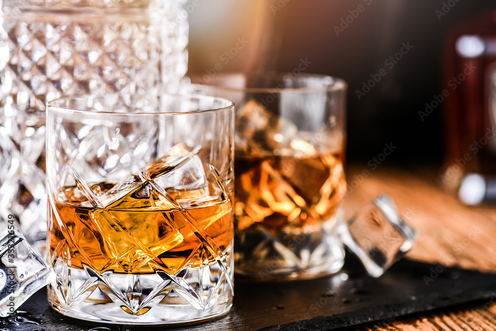 Whiskey with ice in glasses on rustic wood background. Alcohol or spirit from old barrel.
