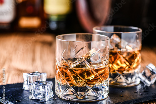 Whiskey with ice in glasses on rustic wood background. Alcohol or spirit from old barrel.