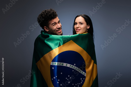 multicultural couple of smiling football fans with brazil flag on grey