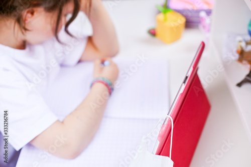 Distance learning online education. Schoolgirl studying at home with digital tablet and doing school homework. Training books and notebooks . Studying online. Soft focus  focus only on the tablet.