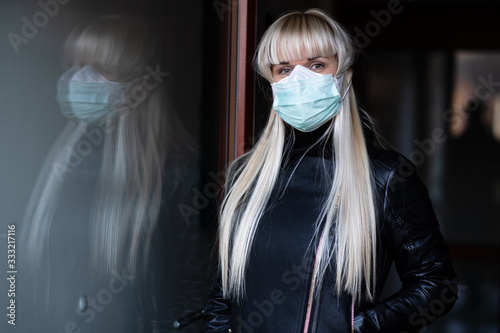 Lovely blond haired caucasian lady protecting herself from viruses while wearing special mask on doorway photo