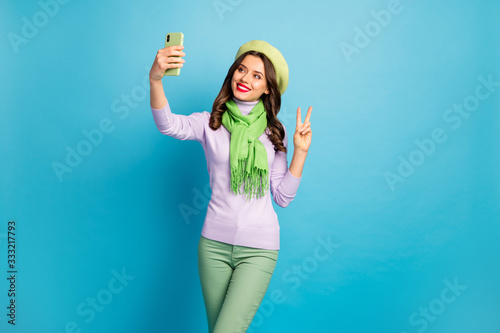 Photo of funny charming lady hold telephone making selfies showing v-sign symbol wear trendy green beret purple turtleneck scarf pants isolated blue color background