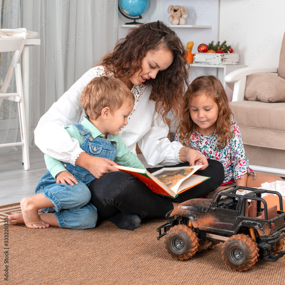 Φωτογραφία Young mother or nanny with small children, a boy and a girl, sit on the floor on