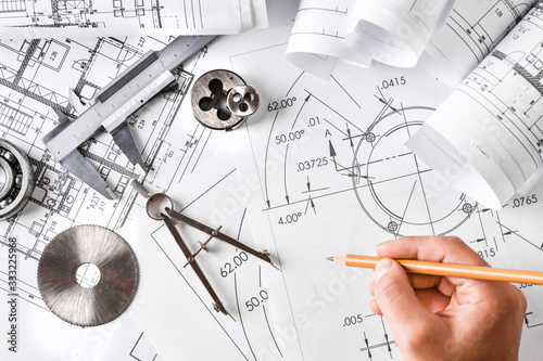 Engineer technicial drawings and mechanical parts engineering industry work project paper prints. Projectant hand with pencil, measuring tools on table. photo