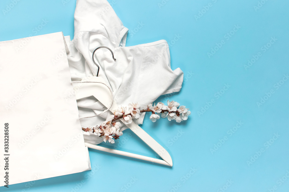 Creative spring sale concept. White wooden hangers with spring flowers white shirt paper bag on blue background top view flat lay. Fashion spring discounts shopping sale store promo design Creative spring sale concept. White wooden hangers with spring flowers white shirt paper bag on blue background top view flat lay. Fashion spring discounts shopping sale store promo design