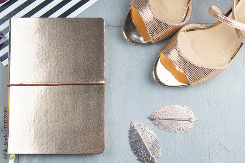 A gold notebook with women's shoes, tulips, glasses and a watch on a concrete background. Flet lay photo