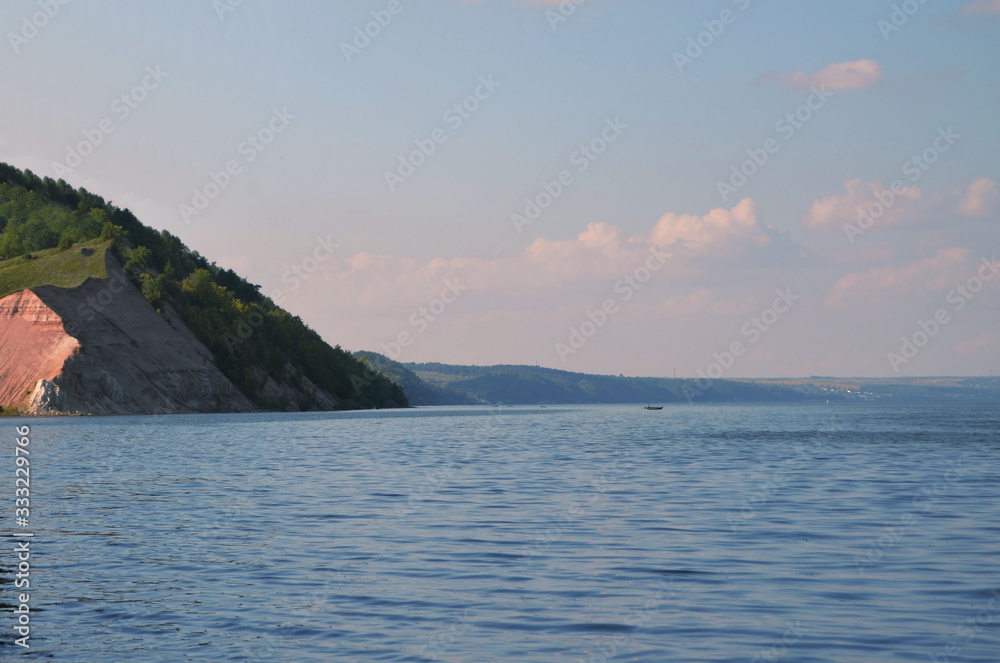 river and steep sandy shore at sunset with fishermen in a boat in the far