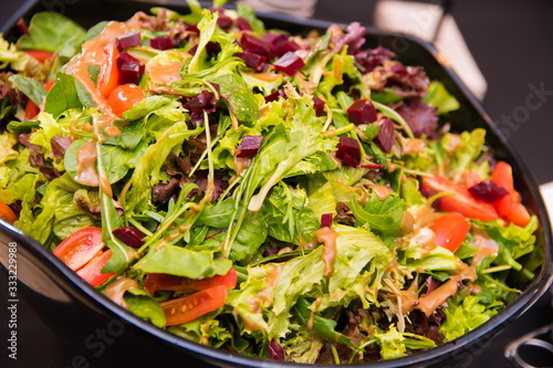Green vegetable salad with a variety of lettuce, spinach, tomato, beetroot, arugula, nuts with a balsamic vinegar dressing in a black bowl