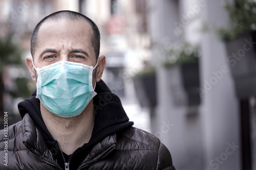Ritratto stretto di un uomo rasato con giubotto scuro  mascherina protettiva chirurgica su sfondo urbano photo